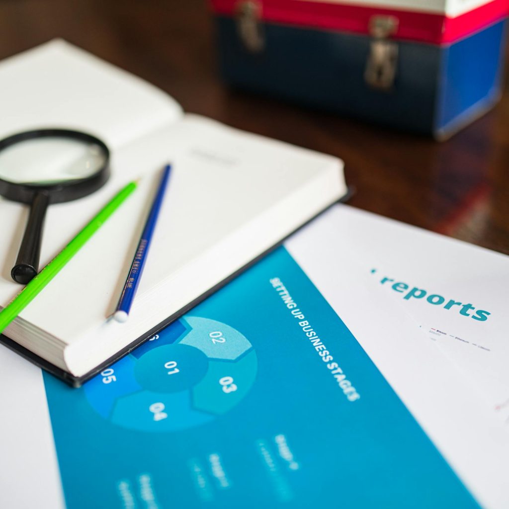 Open book with magnifying glass, pencils, and a business report on a wooden desk.